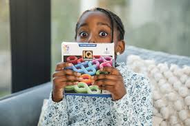 Criança surpreendida a segurar a caixa do jogo de lógica IQ Noodles à frente do rosto, indicando diversão e envolvimento.