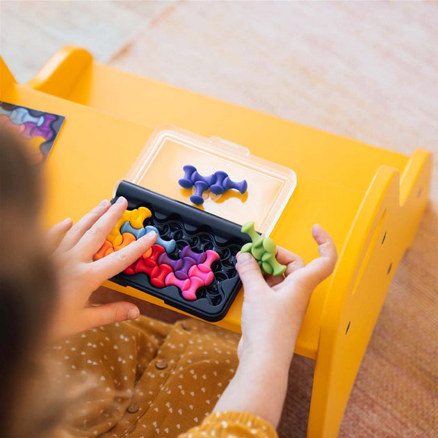 Criança a jogar o IQ Waves, colocando peças coloridas na grelha de encaixe do jogo portátil.