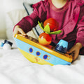 Criança brincando com o navio pirata magnético na cama, mostrando o seu tamanho e a facilidade de uso.