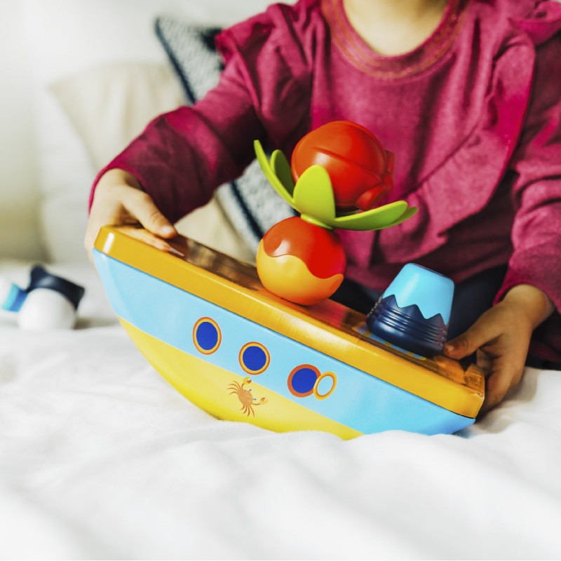 Criança brincando com o navio pirata magnético na cama, mostrando o seu tamanho e a facilidade de uso.