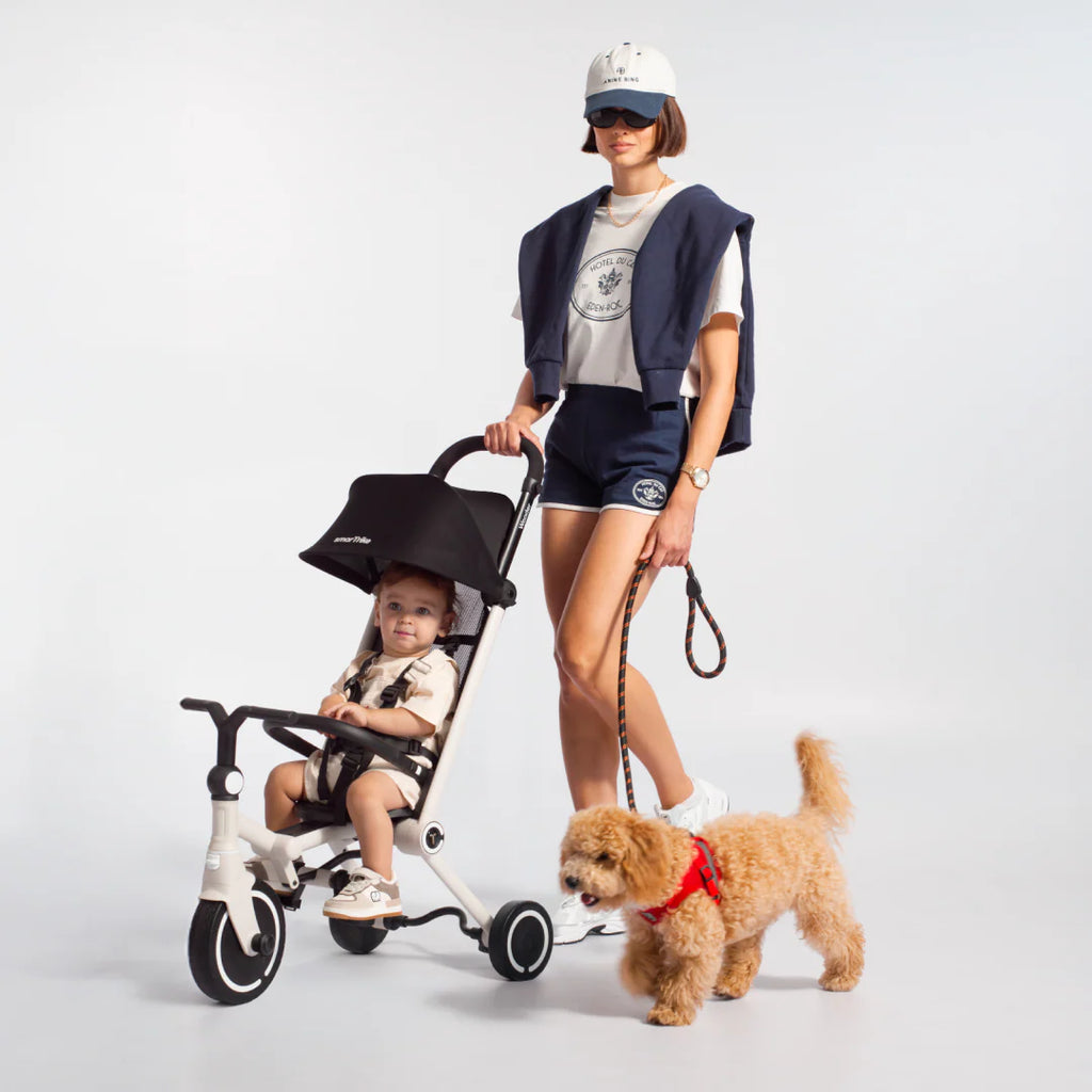 Mãe jovem com estilo a passear o bebé no SMARTRIKE Wonder, um carrinho ultraleve, com um cão pequeno ao lado.