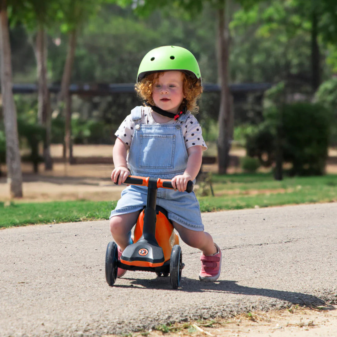Bebé com capacete verde sentado na trotinete Smartrike Xtend, utilizando-a como um veículo de passeio (ride-on) com apoio para os pés.