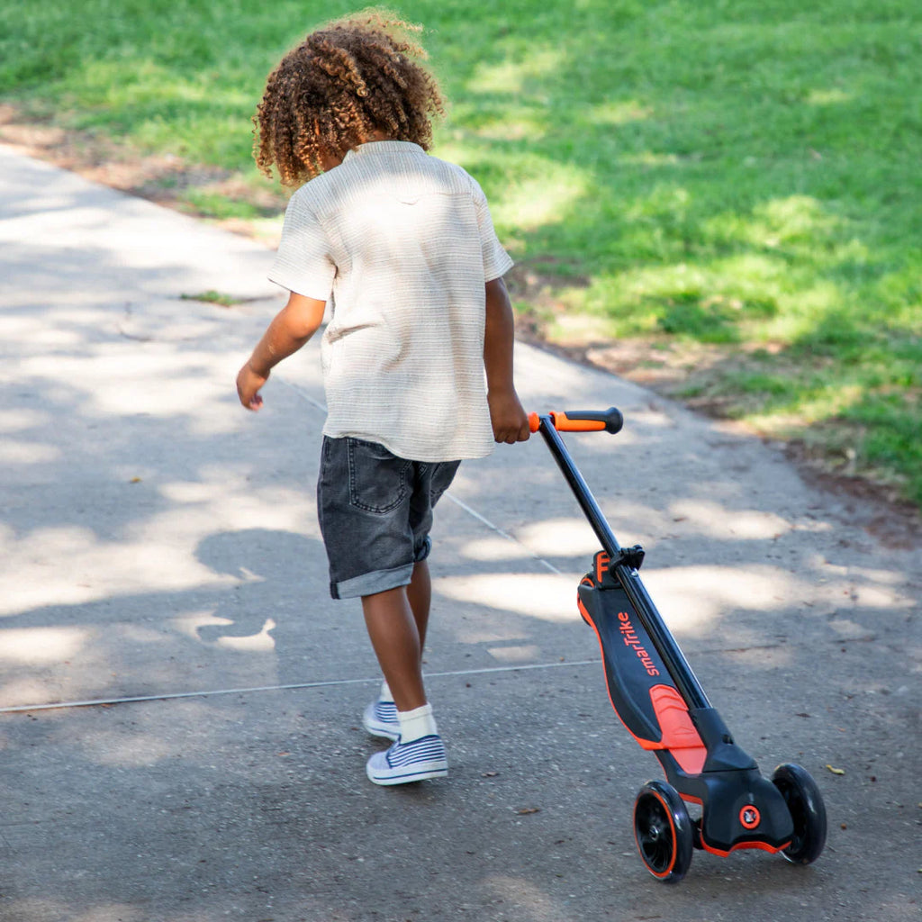 Criança de costas a puxar a trotinete Smartrike Xtend dobrada, que funciona como carrinho de puxar, num caminho de passeio.
