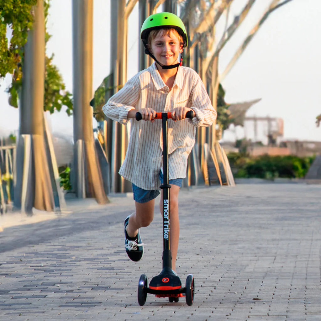 Rapaz mais velho a andar de trotinete Smartrike Xtend, com rodas LED acesas, num passeio pavimentado ao ar livre.