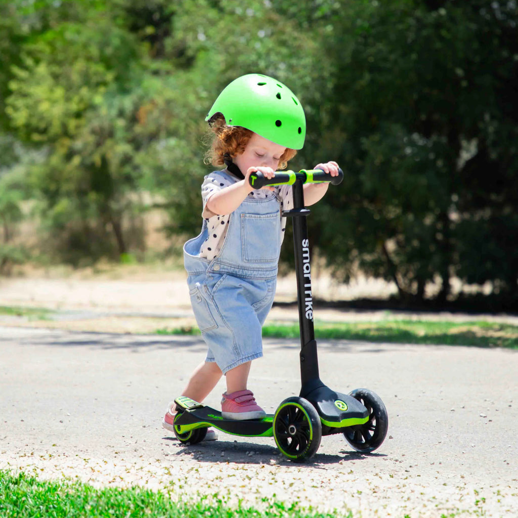 Criança com capacete verde a usar a Smartrike Xtend como trotinete independente, em modo de pé, num caminho exterior.