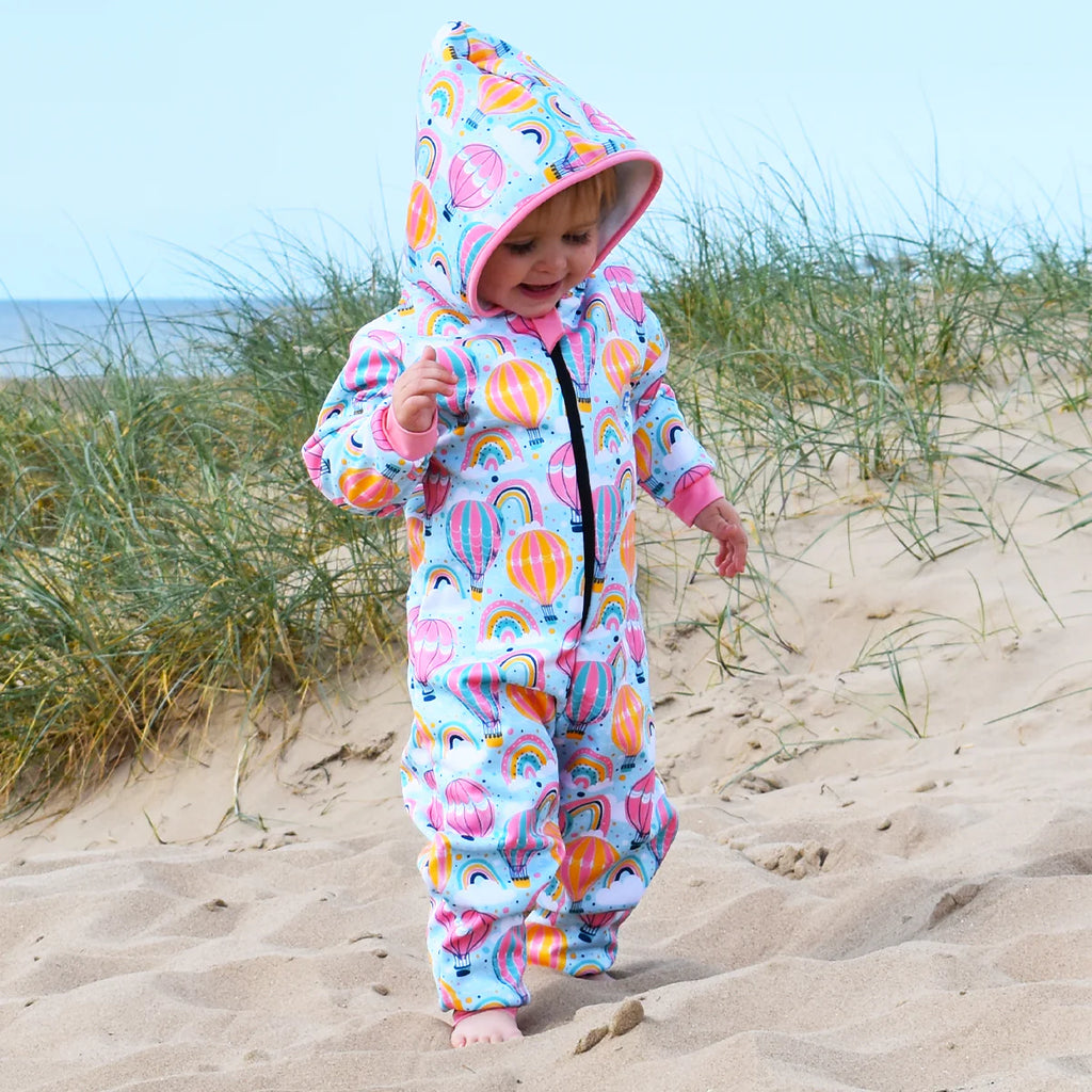 Babygrow impermeável Splash About para pós-natação, cor branca com padrão de balões de ar quente coloridos e arco-íris.