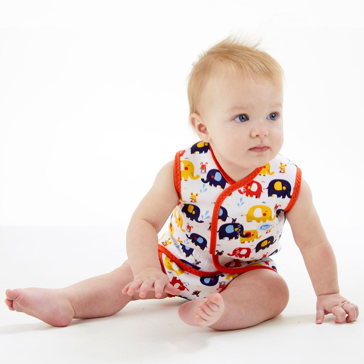 Bebé de cabelo louro sentado no chão, vestindo o fato térmico Baby Wrap™ de elefantes, com focagem no conforto e liberdade de movimentos.