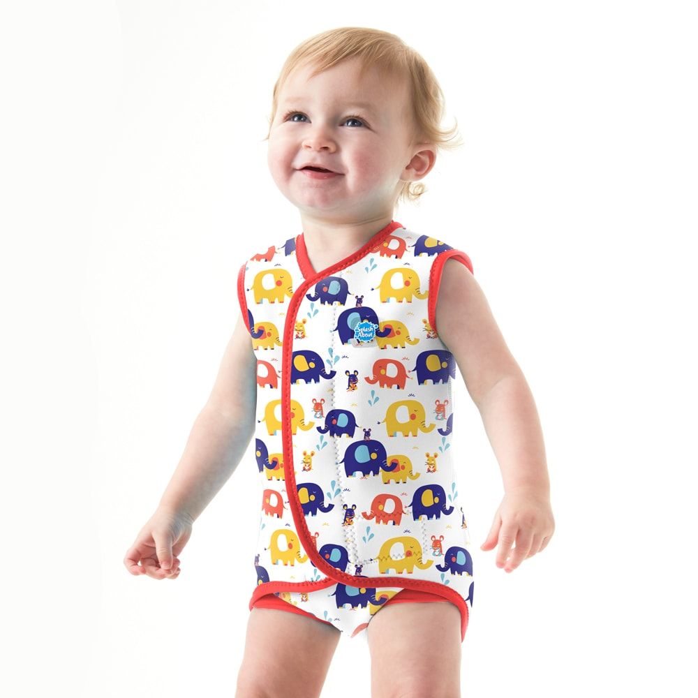 Bebé sorridente em pé, vestindo o fato de piscina térmico Baby Wrap™ com padrão de elefantes, destacando o uso prático.