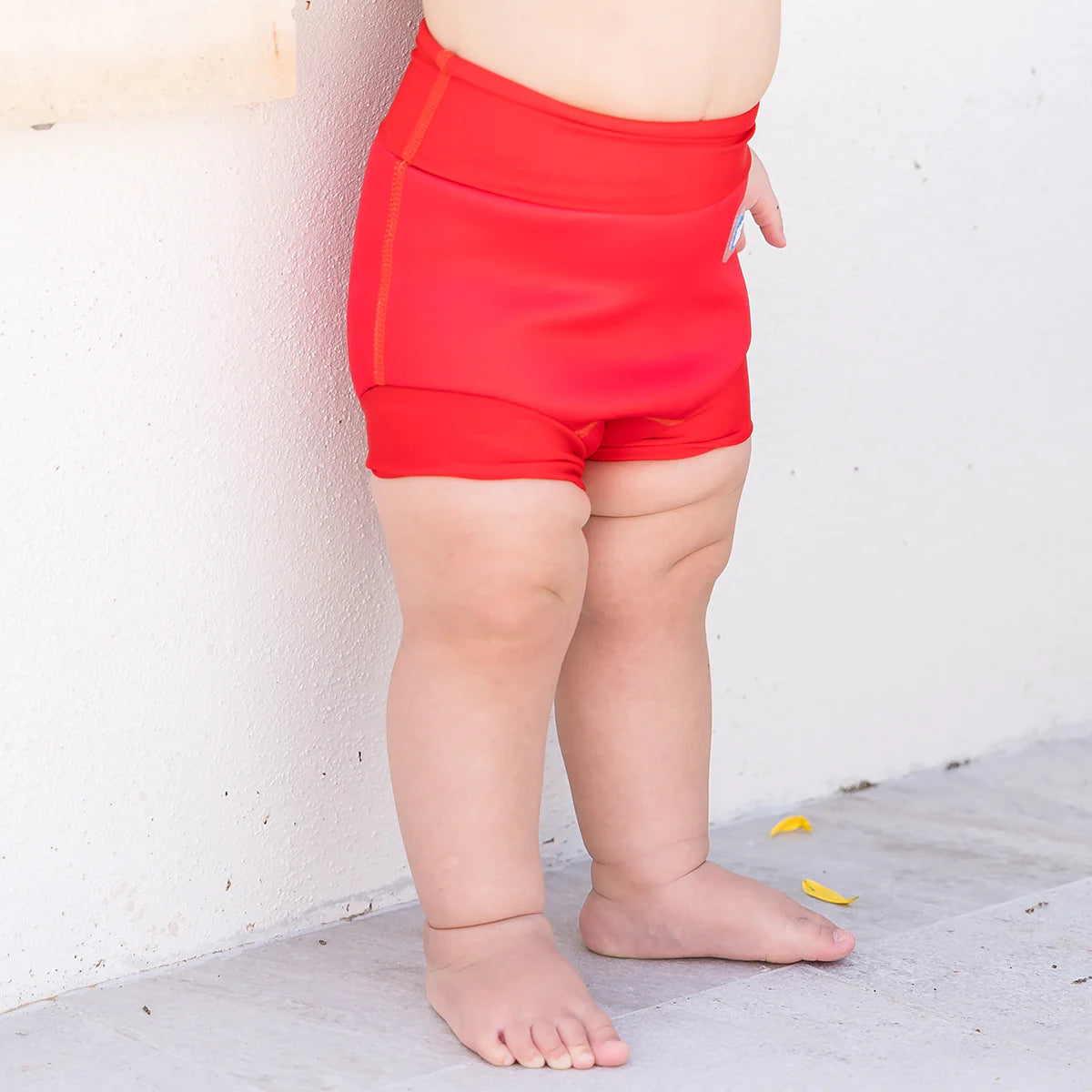 Detalhe do ajuste da fralda de natação Happy Nappy vermelha nas pernas e cintura de um bebé.