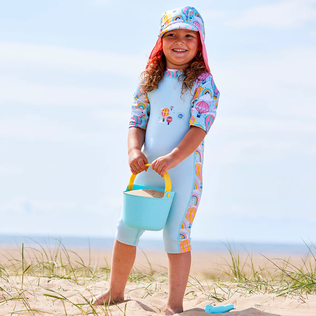 Criança a brincar na água com o fato térmico Splash About Up & Away, destacando a flexibilidade dos painéis de Lycra nos braços.