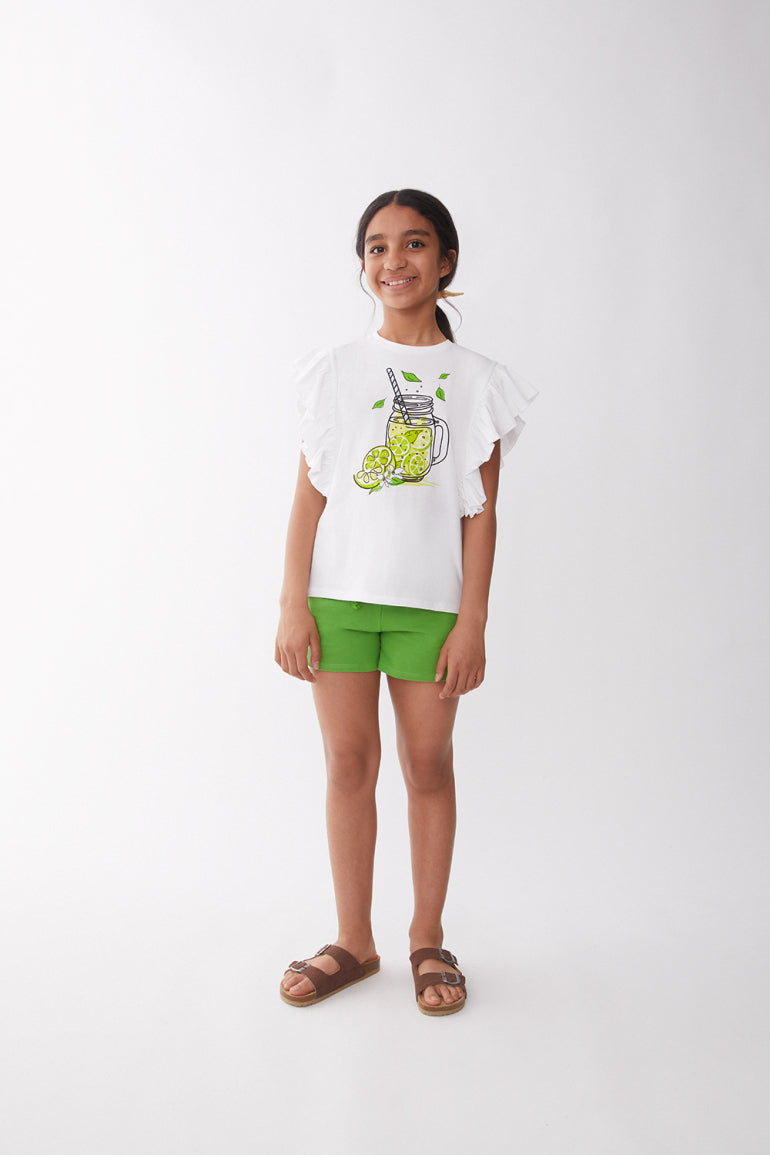 Menina sorridente veste o conjunto Street Monkey: t-shirt branca com estampa de limonada e shorts verdes, ideal para o verão.