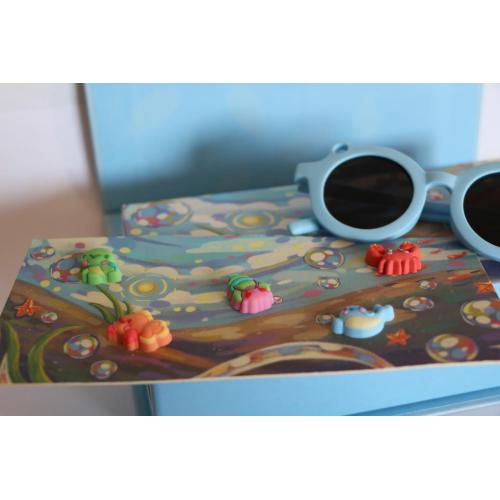 Detalhe dos óculos de sol infantis Sumsun azuis e acessórios "Summies" de temática marinha sobre o cartão de exposição.