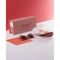 Conjunto de óculos de sol infantis Sumsun cor de terracota com caixa, pano de limpeza e acessórios decorativos sobre fundo branco e vermelho.
