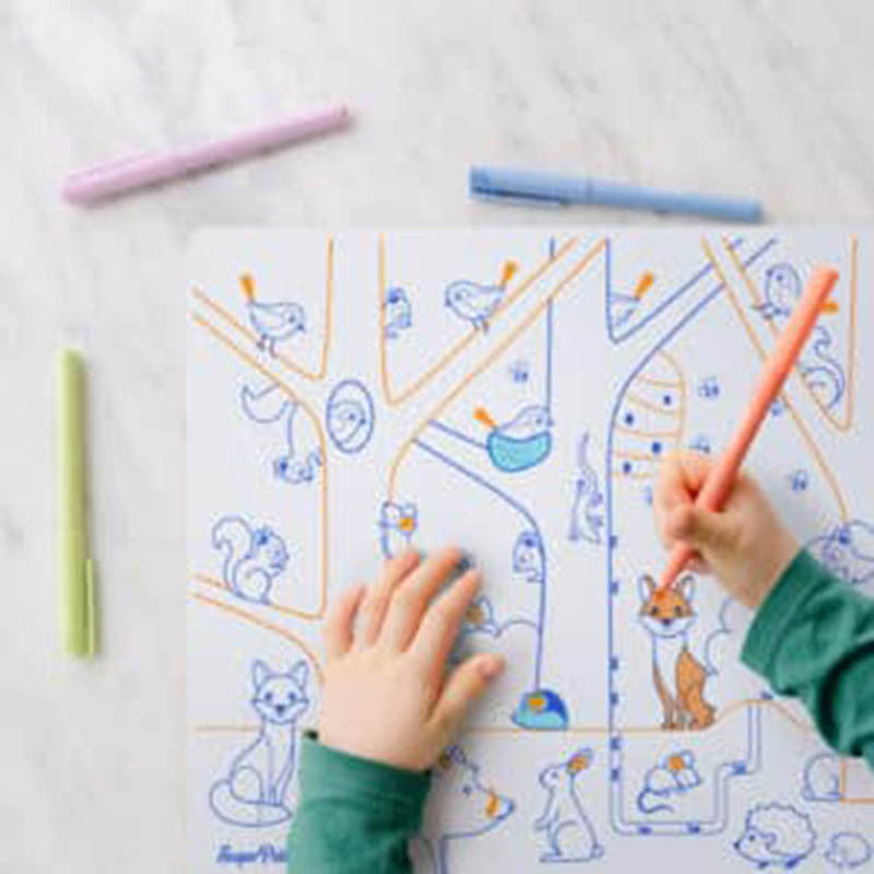 Criança a colorir um tapete de silicone educativo da SuperPetit com um marcador cor de salmão, rodeado por marcadores de cores vivas.