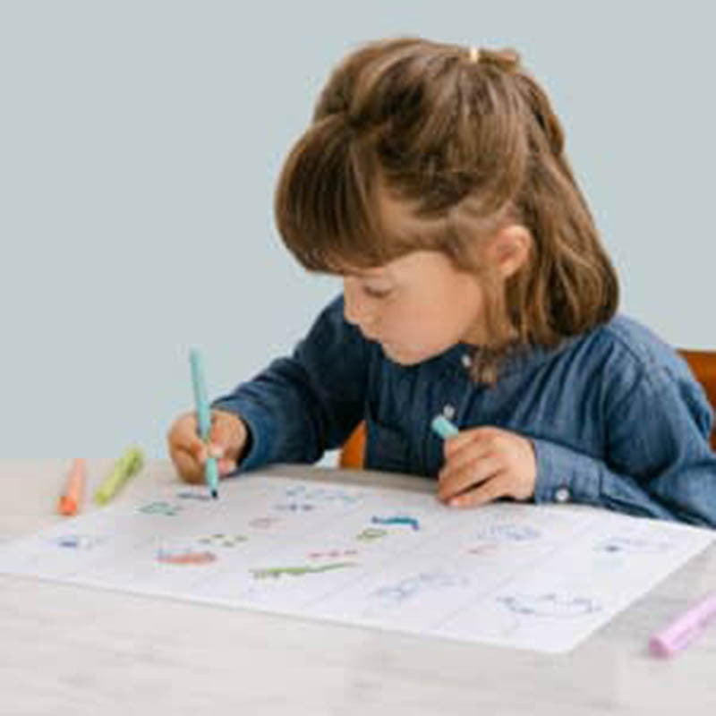 Menina concentrada a usar um marcador azul claro para colorir o tapete educativo de silicone SuperPetit sobre uma mesa.