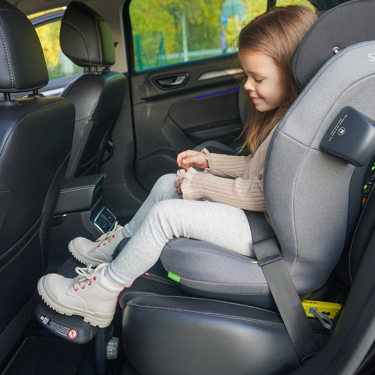 Criança sentada confortavelmente num assento auto cinzento, com as pernas apoiadas no apoio universal Swandoo instalado no carro.