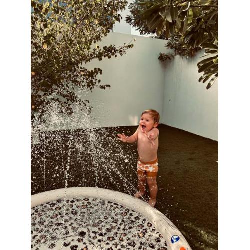 Criança pequena a brincar num tapete de esguichos inflável Swim Essentials com design de leopardo, num jardim.