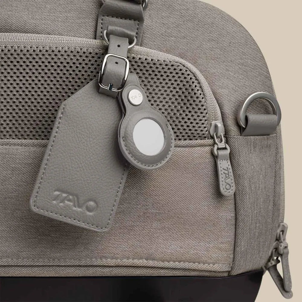 Detalhe do acessório de couro vegan TAVO com suporte para localizador (tipo AirTag) pendurado no transportador cinzento.