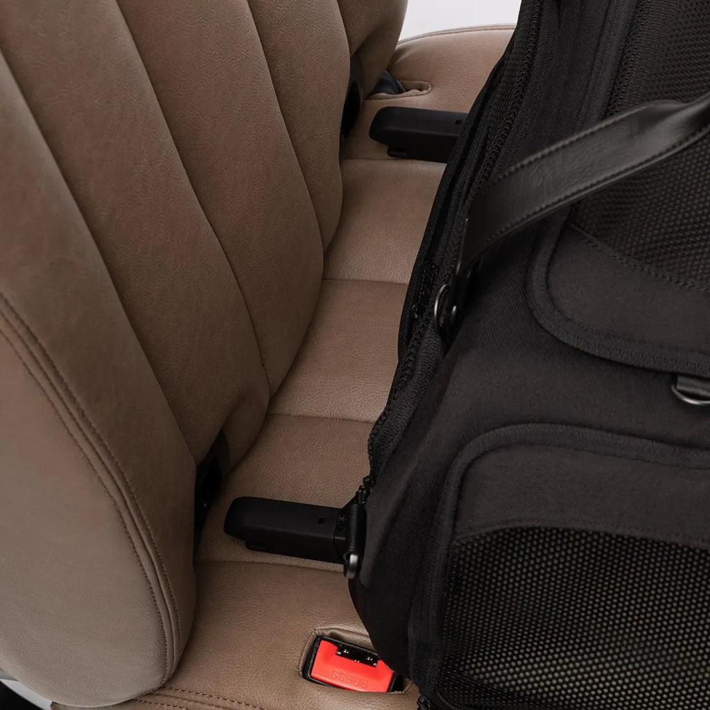 Transportador TAVO Dupree II preto instalado no banco traseiro do carro, ao lado do assento de couro bege, com conectores ISOFIX visíveis.