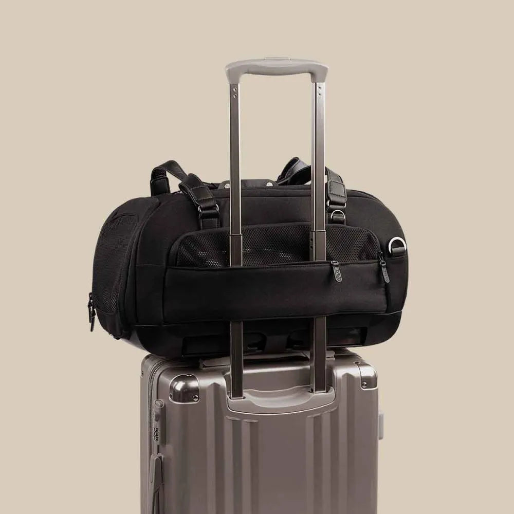 Transportadora TAVO Dupree II preta pousada sobre a pega extensível de uma mala de viagem prateada, demonstrando a funcionalidade de encaixe para aeroporto.