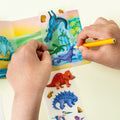 Close-up de mãos de criança a usar o conjunto Tiger Tribe Mini Transfer Magic Dinosaurs, focando no detalhe da transferência do autocolante.