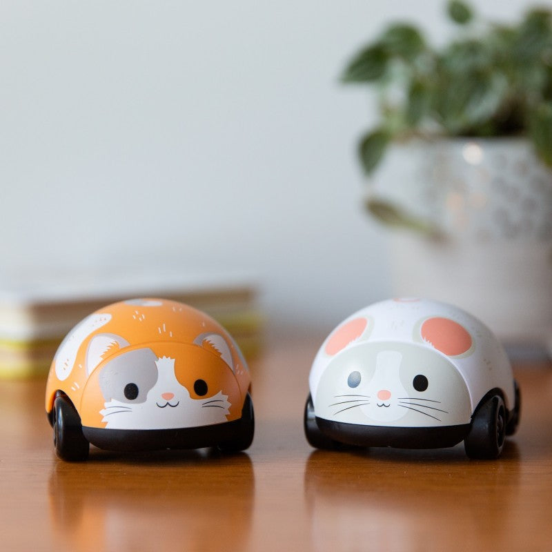 Brinquedos Gato e Rato Pull Backs da Tiger Tribe em primeiro plano sobre um chão de madeira, com planta desfocada ao fundo.