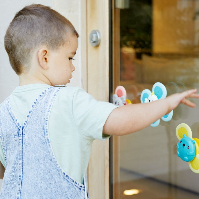 Criança pequena a brincar com os três Sensory Spinners fixados numa superfície de vidro lisa, estimulando a coordenação motora.