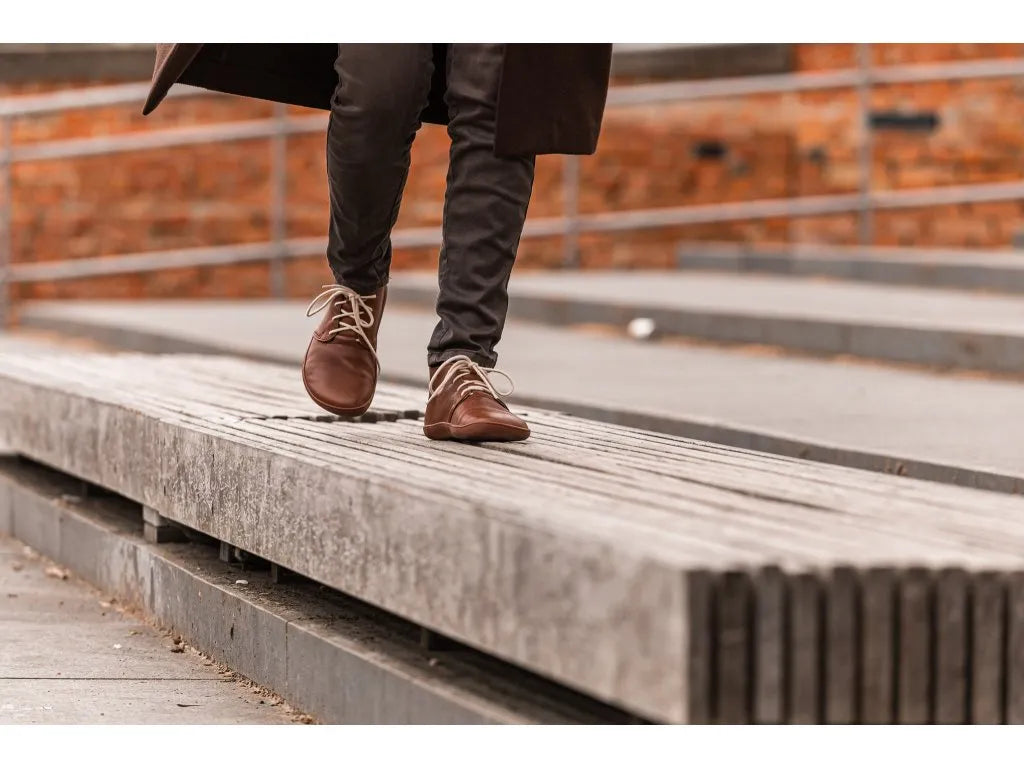 Mulher a caminhar com botas barefoot TIKSI castanhas, combinando estilo e conforto num ambiente urbano.

