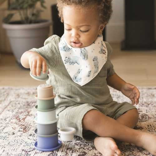 Bebé a brincar com o conjunto de 7 vasos empilháveis de silicone Tiny Twinkle em tons suaves, estimulando a coordenação motora.