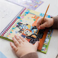 Criança a usar a caneta de raspar no livro de atividades Bluey, revelando o desenho por baixo da camada preta.