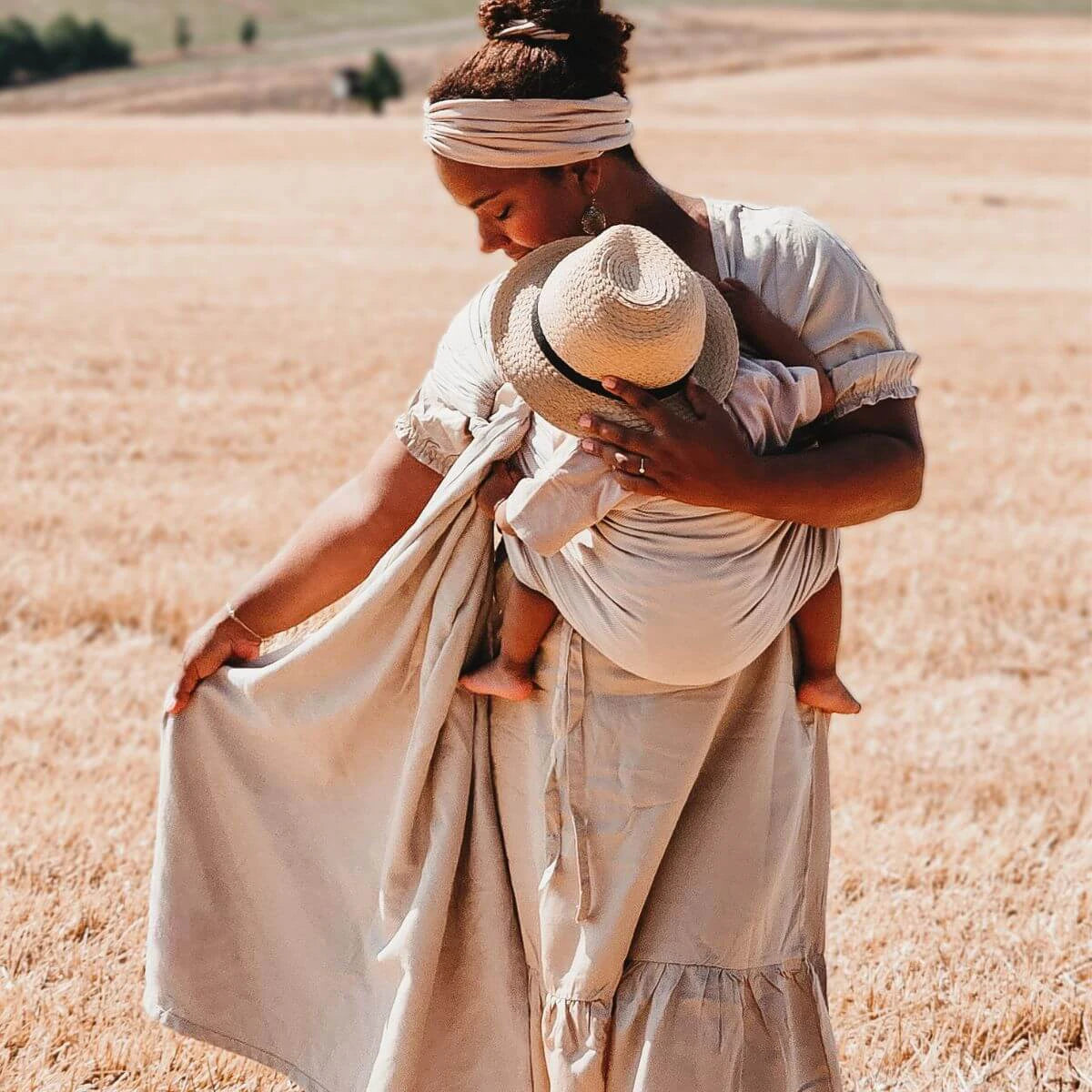 Mãe usando um sling de argolas Hoppediz num campo aberto, carregando o seu bebé de forma confortável e segura.