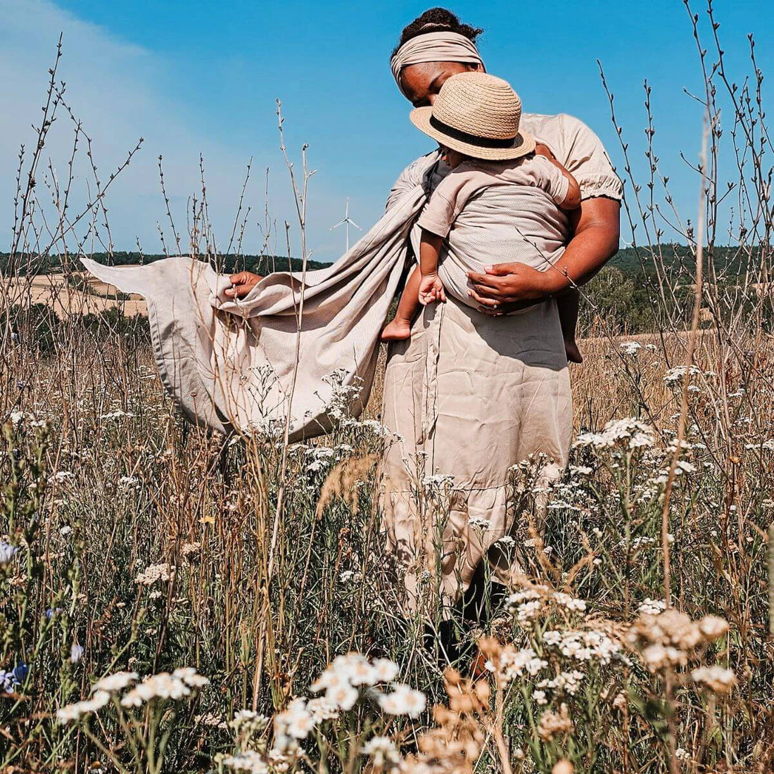 Mãe usando um sling de argolas Hoppediz num campo aberto, carregando o seu bebé de forma confortável e segura.