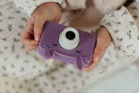 Mãos de criança a segurar a máquina fotográfica digital Hoppstar Rookie Blossom roxa, com o seu design de coelho e capa de silicone protetora.