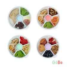 Quatro lancheiras GoBe Snack Spin de 21 cm, cada uma com cinco compartimentos preenchidos com diferentes lanches saudáveis e coloridos.