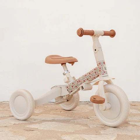 Triciclo Little Dutch em modo de bicicleta de equilíbrio (draisiana) com assento ajustado, em ambiente exterior com chão de pedra.