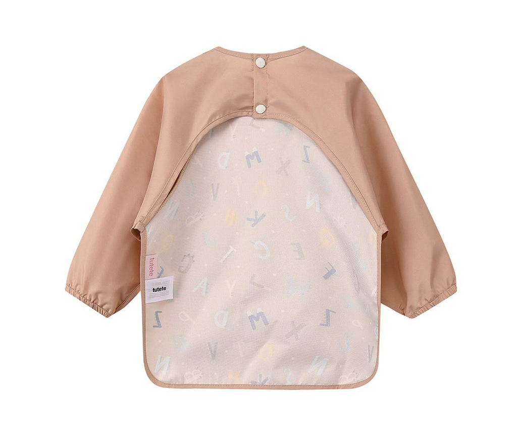 Vista traseira do babete Tutete com mangas em cor bege, destacando o design de costas abertas e fecho de molas.
