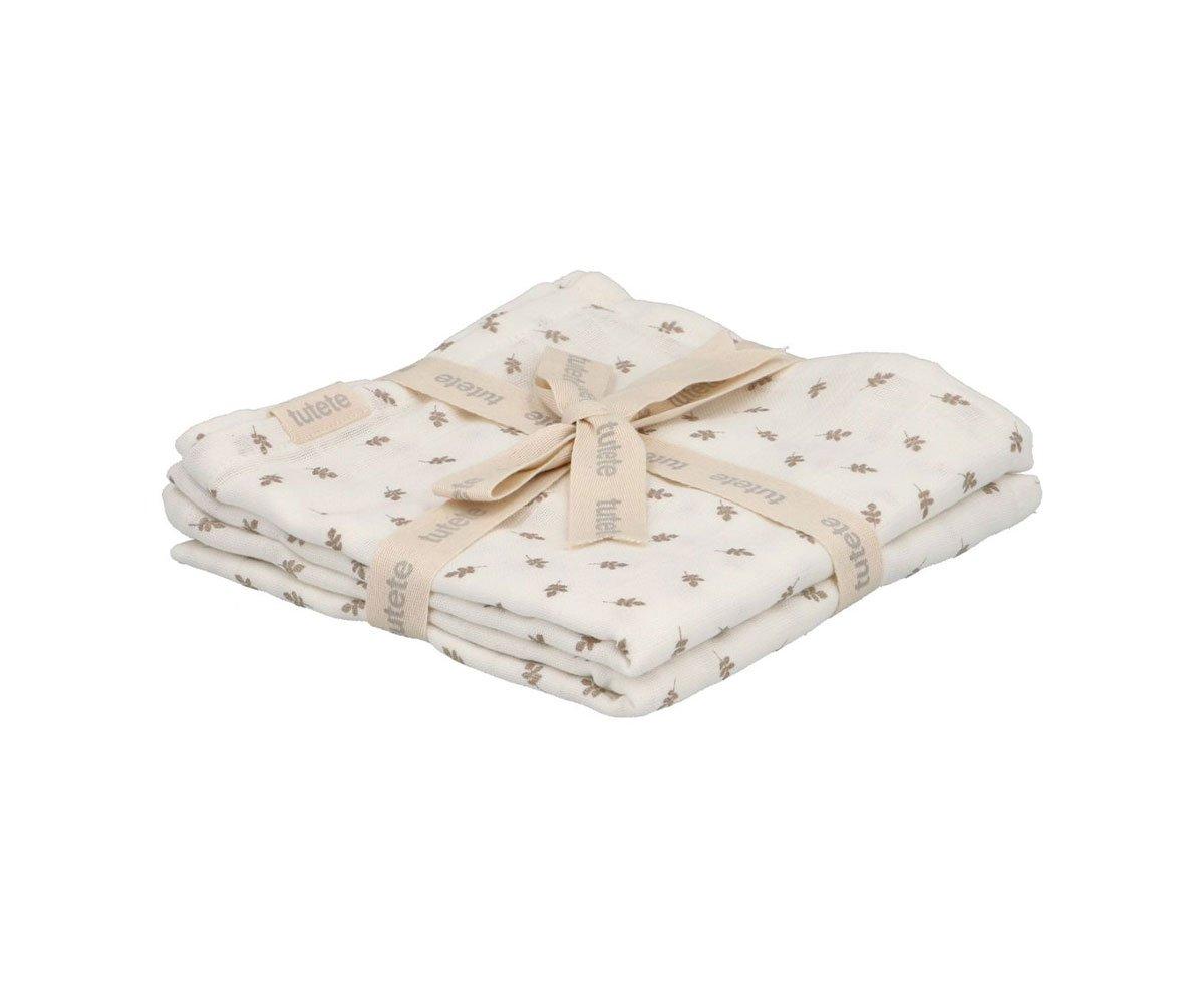 Conjunto de 2 musselinas Lassig 100% algodão, dobradas e atadas com fita bege com a marca "tutete", apresentando padrão discreto de folhas castanhas.