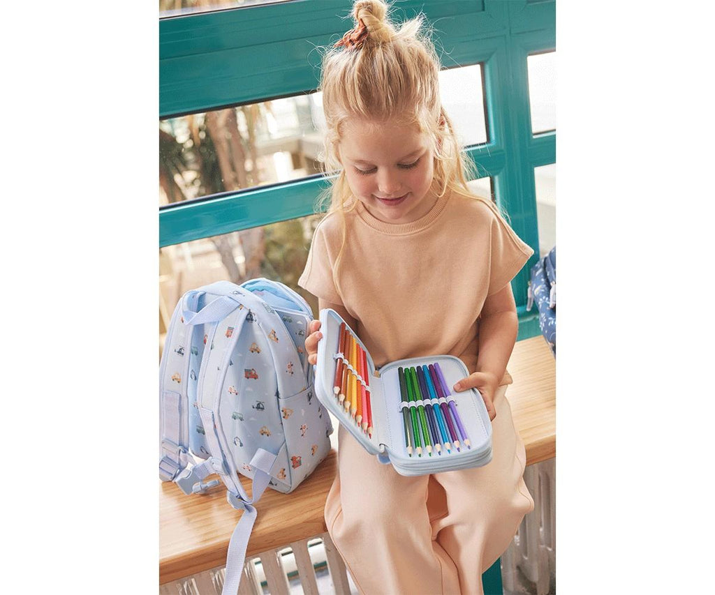 Criança loira a sorrir, a segurar o estojo plumier duplo Tutete aberto, cheio de lápis de cor, ao lado de uma mochila azul clara.