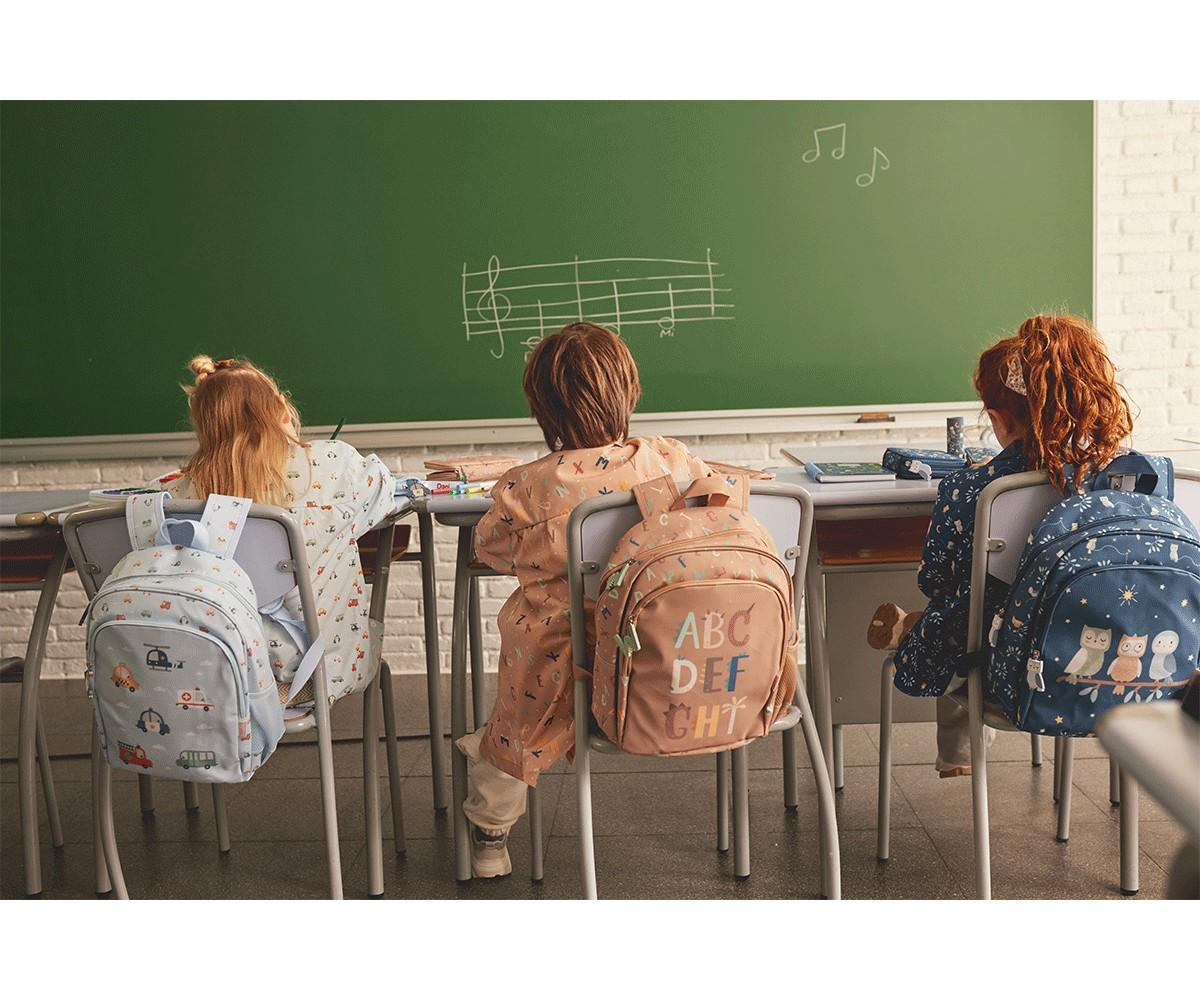 Três crianças sentadas em sala de aula com mochilas Tutete diferentes, incluindo o modelo Funny Letters bege.