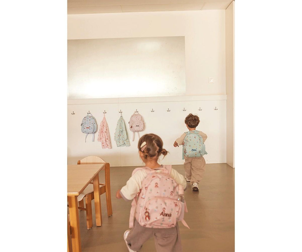 Crianças com mochilas personalizadas Tutete (rosa e azul) a entrar numa sala de aula com casacos pendurados nos ganchos.