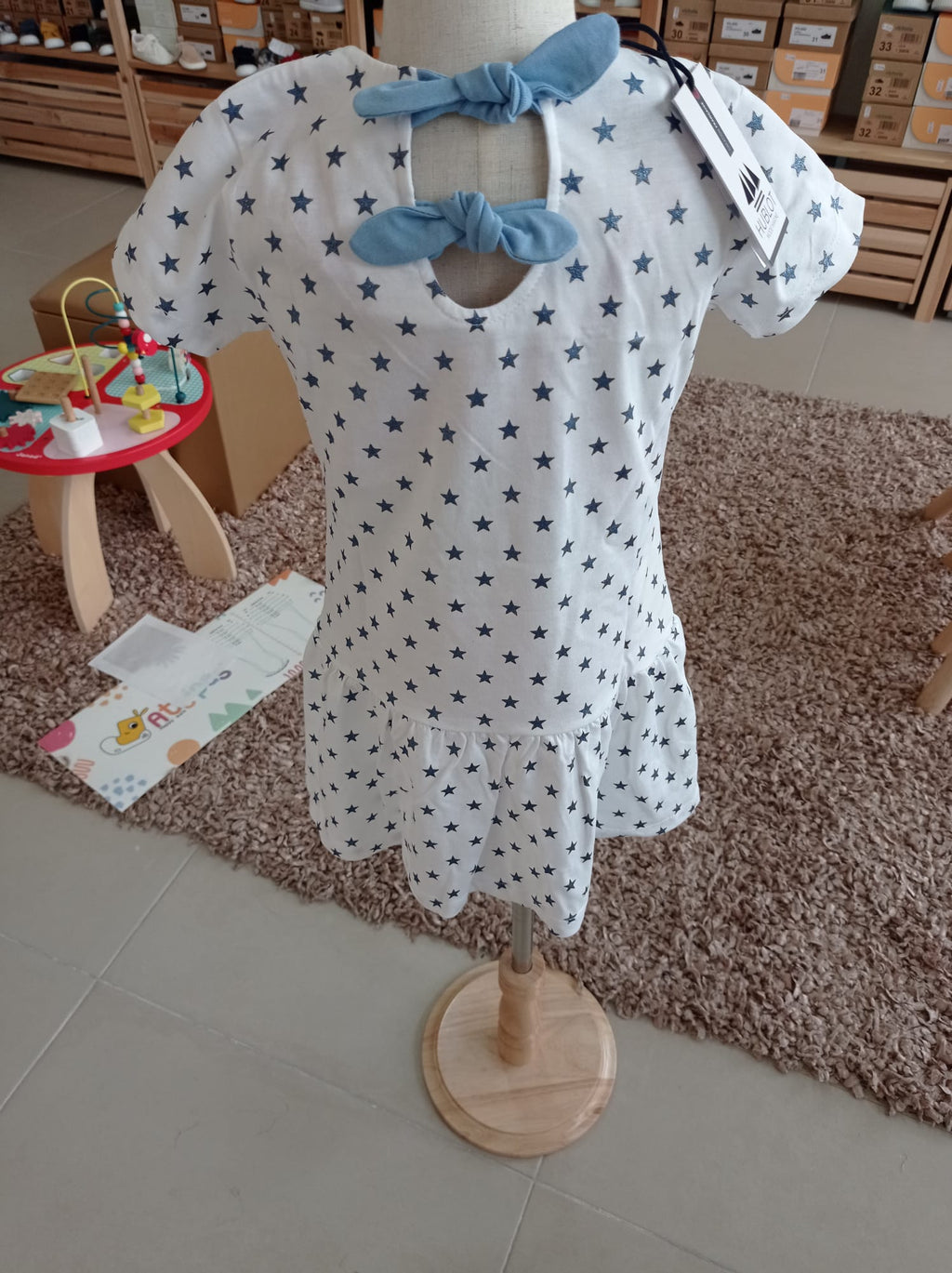 Vista traseira do vestido infantil Hublot, destacando os dois laços azuis ajustáveis que fecham a abertura superior das costas.