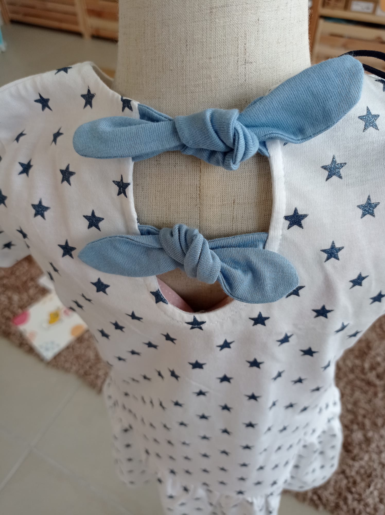 Detalhe aproximado dos laços azuis amarrados nas costas do vestido Hublot, sobre o tecido estampado com estrelas.
