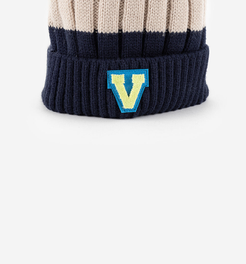 Detalhe do aplique "V" da marca Victória no rebordo em malha do gorro Victoria azul marinho.