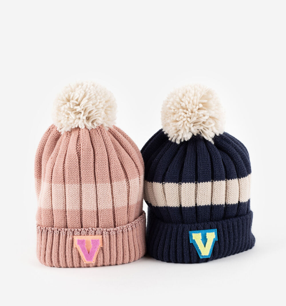 Dois gorros Victoria para criança, um em tons de rosa e outro em azul marinho, com pompons e apliques da marca "V".