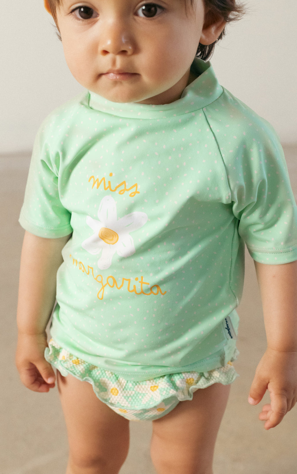 Criança pequena a usar a camisola de manga curta UV verde com estampa de flor, ideal para praia e piscina.