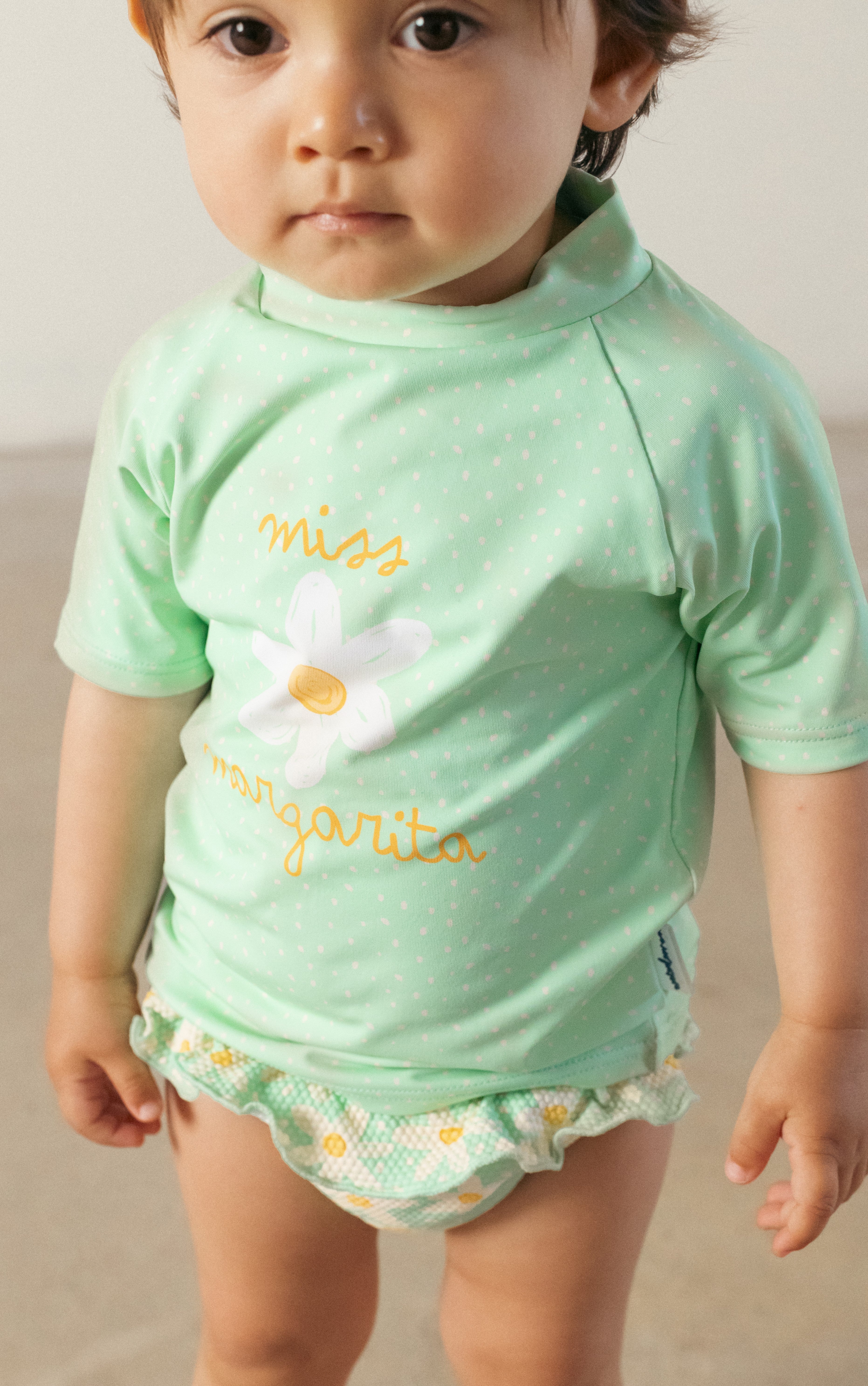 Criança pequena a usar a camisola de manga curta UV verde com estampa de flor, ideal para praia e piscina.