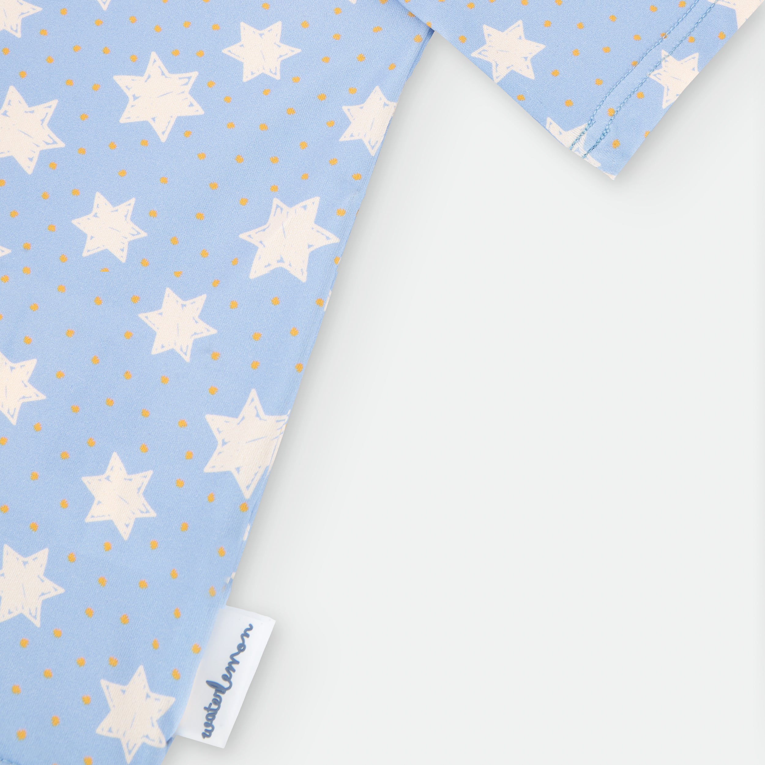 Detalhe em close-up da costura raglan e da etiqueta Waterlemon na bainha da camisola de proteção solar com padrão de estrelas.