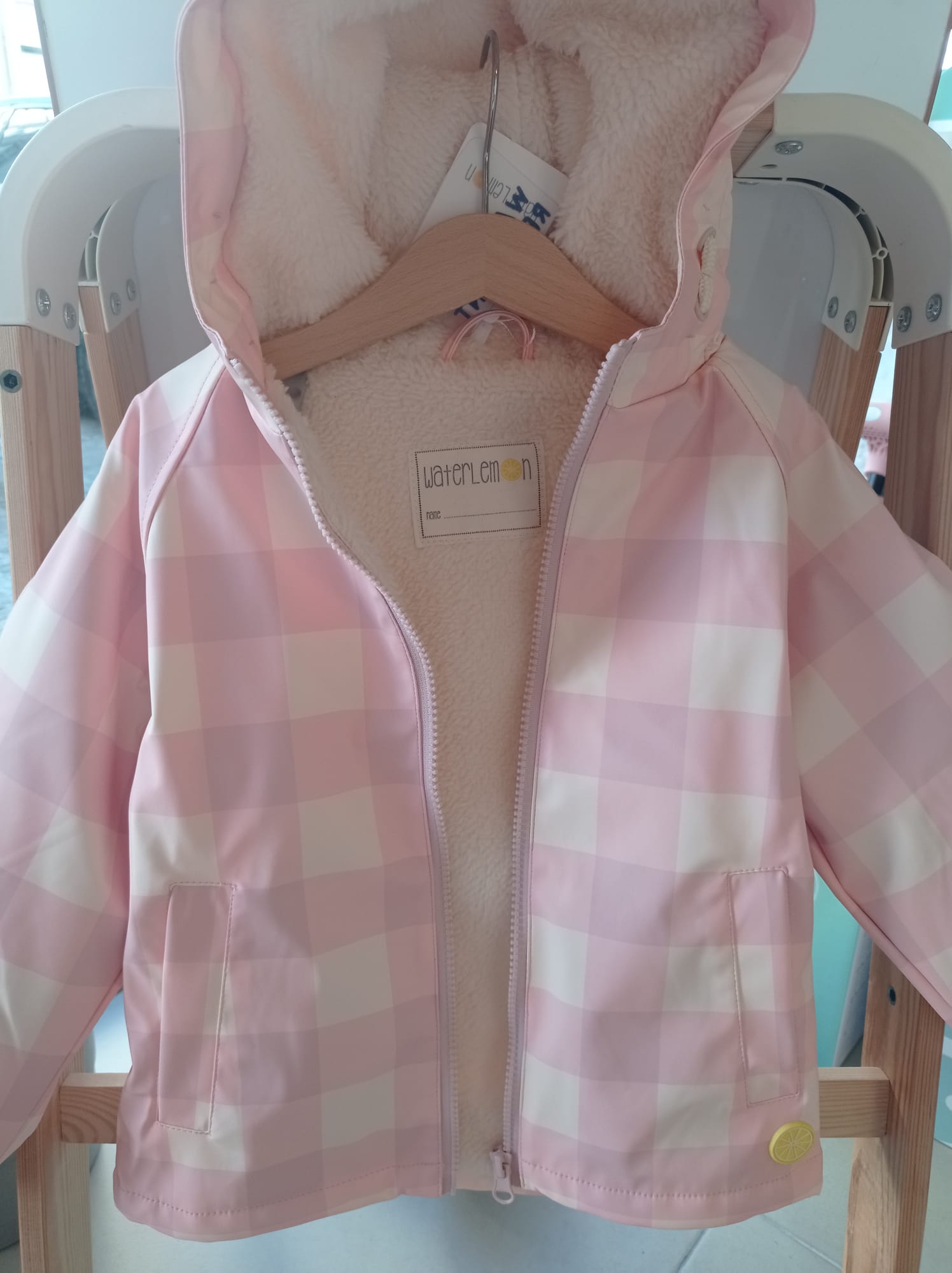 Criança a usar o casaco polar impermeável Waterlemon xadrez rosa, em pose de brincadeira ao ar livre.
