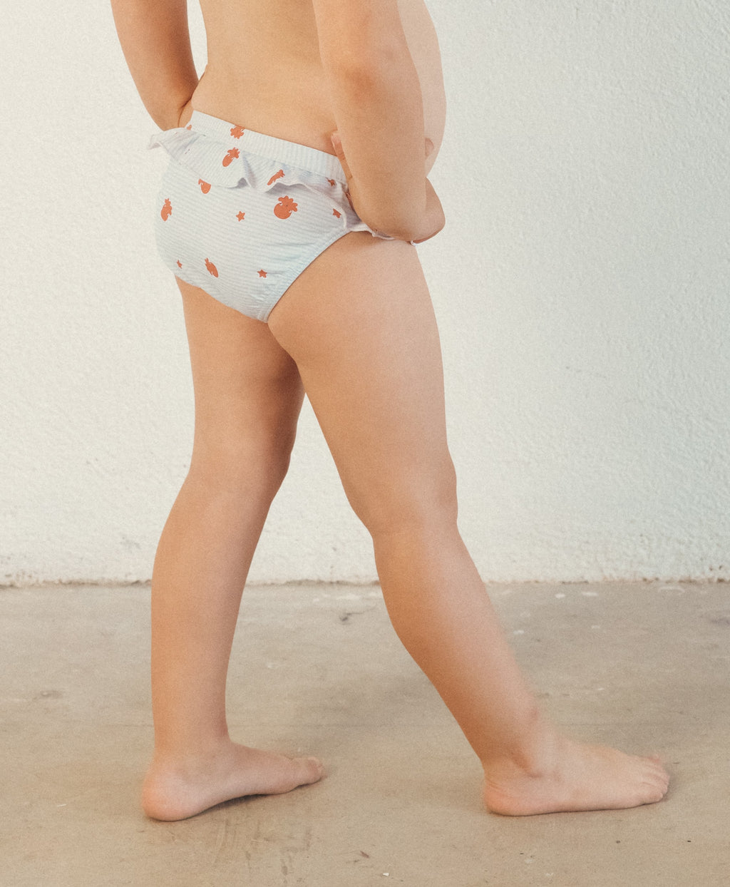 Vista lateral de criança a usar a cueca de banho Waterlemon, evidenciando o corte, o folho e os laços laterais.