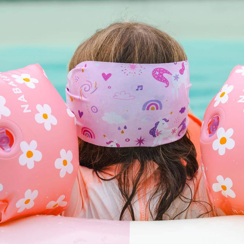 Criança na água com a parte de trás da cabeça visível, usando a banda elástica Waterplops de unicórnios e flutuadores laterais cor-de-rosa.
